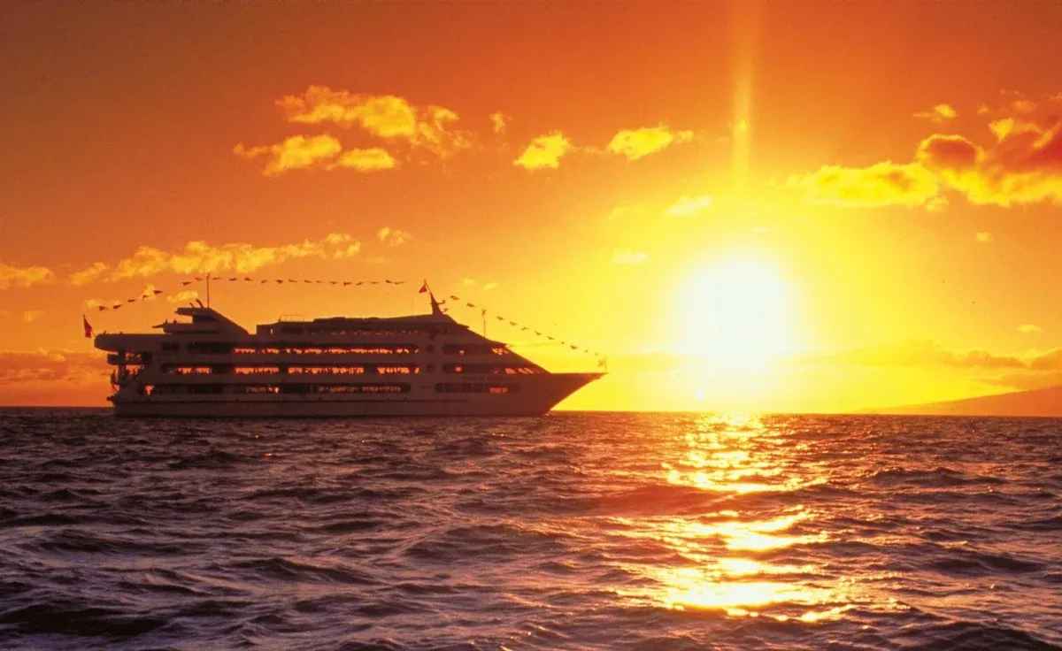 Guests dining at white-linen tables during a sunset dinner cruise in Honolulu off Waikiki with Diamond Head behind